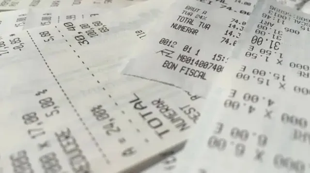 Mai multe bonuri fiscale de hârtie albe sunt împrăștiate pe o suprafață, afișând cifre, text și linii de separare negre.