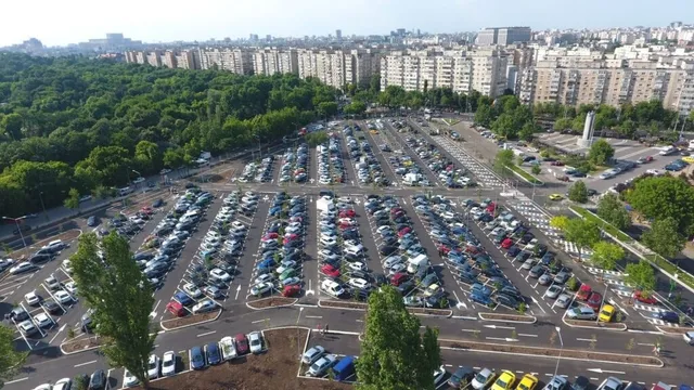 O vedere de sus asupra unui parc verde și a unei parcări mari pline de mașii colorate din diverse unghiuri.