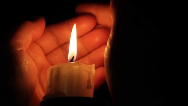 Două mâini țin o lumânare aprinsă într-un mediu întunecat.