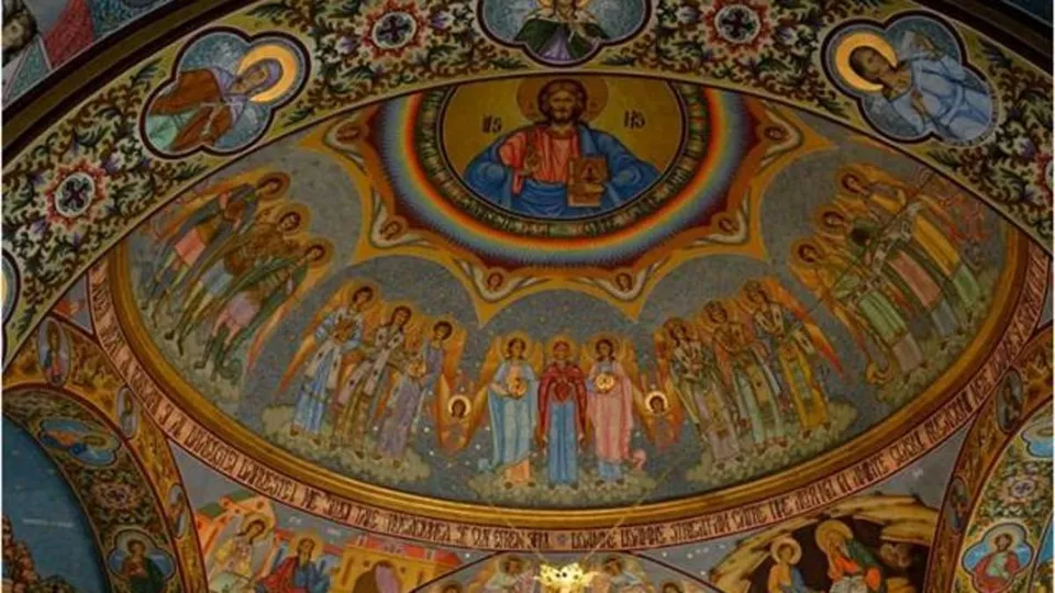 Pictură religioasă pe un dom de biserică reprezentând figuri sfinte și o figură centrală încadrată de un arcbog de culori.