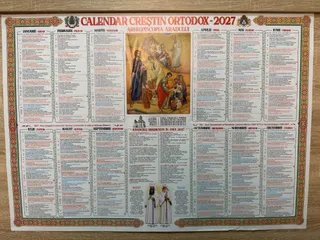 Un calendar de perete cu text și ilustrații religioase este întins pe o suprafață plană de culoare maro.