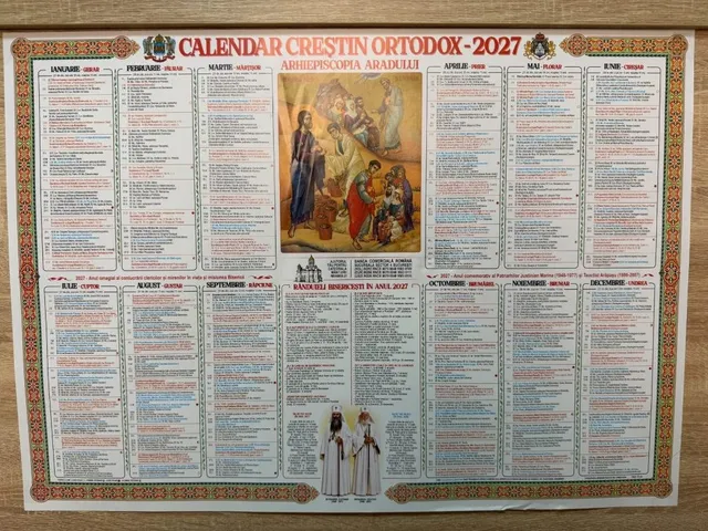 Un calendar de perete cu text și ilustrații religioase este întins pe o suprafață plană de culoare maro.
