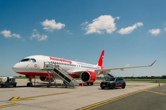 Un avion alb cu detalii roșii și textul AnimaWings stă pe o pistă de beton lângă o mașină neagră sub un cer cu nori albi.