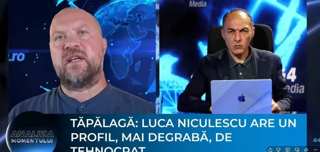 Un bărbat cu barbă și păr scurt este prezentat în prim-plan, în timp ce un alt bărbat stă la un birou cu un laptop în fundal.