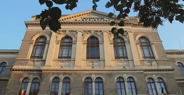 O clădire cu fațadă clasică, ferestre înalte și inscripție pe partea superioară, încadrată parțial de frunze de copac în prim-plan.
