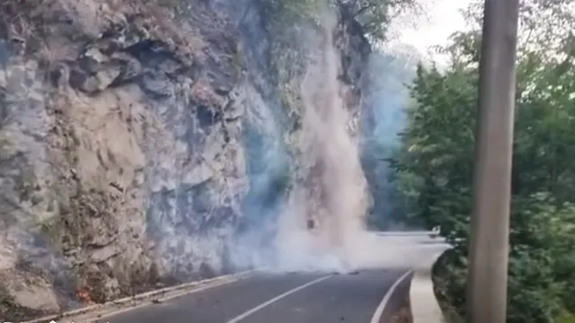 Drum asfaltat curbat trece pe lângă un versant stâncos, unde fum și flăcări mici se văd lângă șosea.