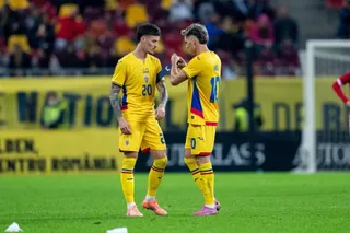 Doi jucători de fotbal îmbrăcați în echipamente galbene stau pe terenul de fotbal, unul privind spre celălalt.