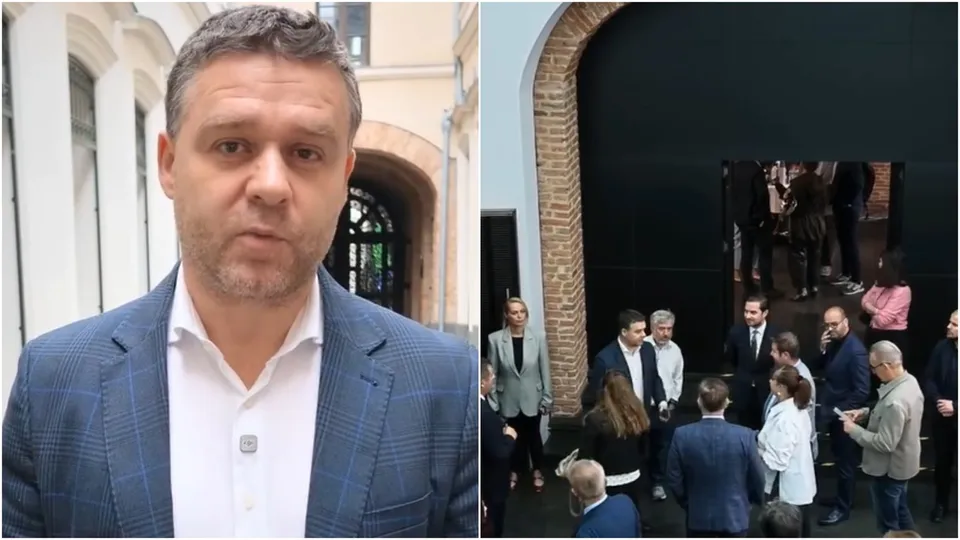 Un bărbat cu sacou albastru și cămașă albă stă în fața unei clădiri, în timp ce în partea dreaptă un grup de persoane stă lângă un perete negru.