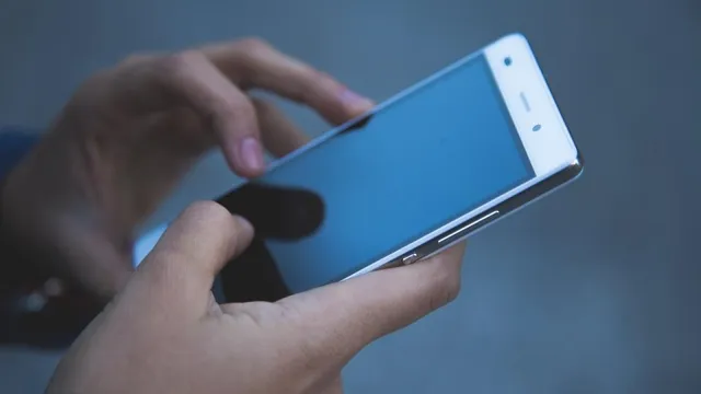 Două mâini țin și utilizează un smartphone cu ecranul aprins într-un cadru cu fundal albastru.