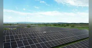 O vedere aeriană a unei centrale solare cu panouri fotovoltaice aranjate pe un câmp deschsub cerul albastru cu nori dispersi.