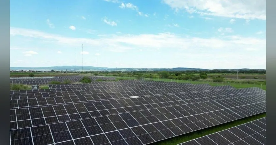 O vedere aeriană a unei centrale solare cu panouri fotovoltaice aranjate pe un câmp deschsub cerul albastru cu nori dispersi.