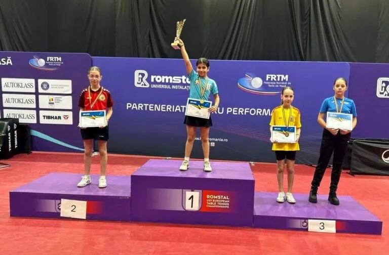 Patru fete stau pe podiumuri de premiere, una ridicând un trofeu și purtând medalii, în timp ce celelalte țin diplome și poartă medalii.