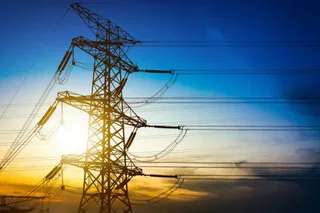 O turn de înaltă tensiune este siluetată în fața unui cer la apus, cu linii electrice întinzându-se orizontal prin cadru.