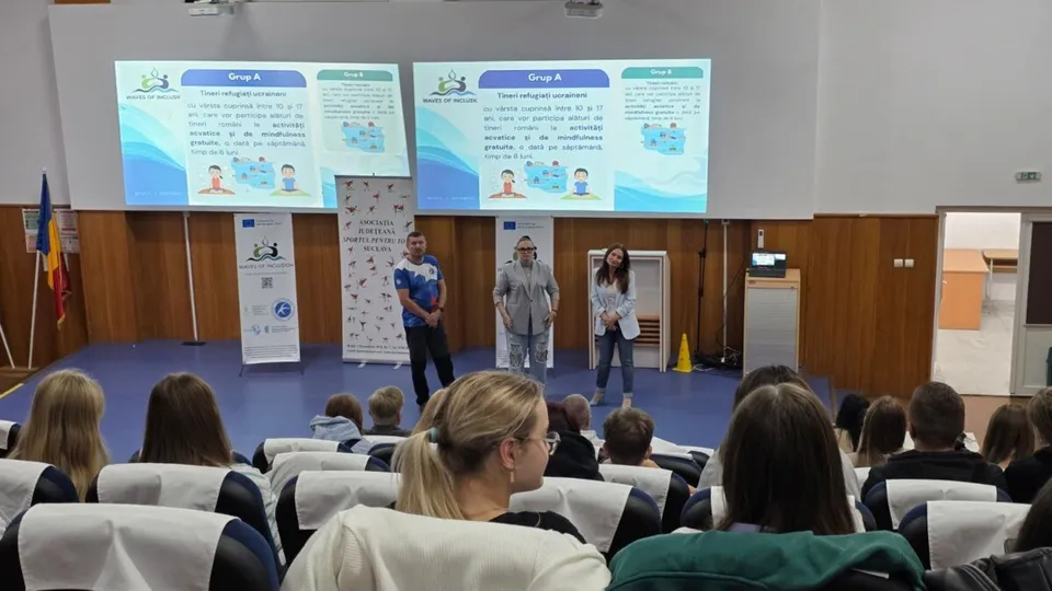 Trei adulți vorbesc în fața unei audiențe de copii și adolescenți, cu două ecrane mari în fundal afișând prezentări despre „Waves of Inclusion”.