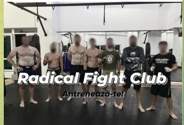 Șapte bărbați stau în rând pe un covor de antrenament într-o sală de sport, purtând pantaloni scurți și tricouri sau fiind toracele dezbrăcat.