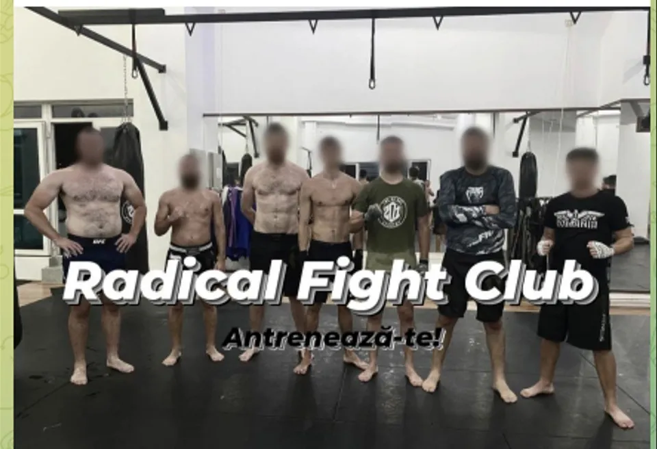 Șapte bărbați stau în rând pe un covor de antrenament într-o sală de sport, purtând pantaloni scurți și tricouri sau fiind toracele dezbrăcat.