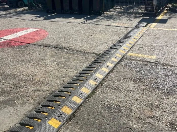 Un dispozitiv de tip bumper negru cu marcaje galbene este montat pe o suprafață asfaltată lângă o zonă marcată cu vopsea roșie și albă.
