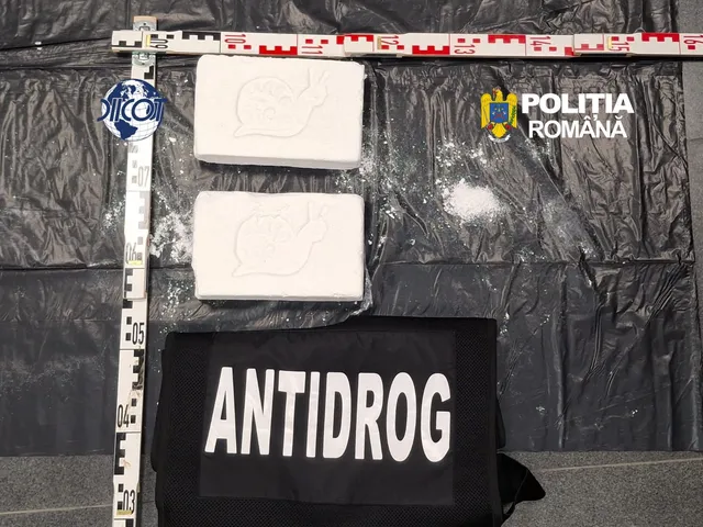 Două pachete albe de droguri și o pungă cu pudră sunt așezate lângă o riglă, pe un fundal negru, cu echipament ANTIDROG.