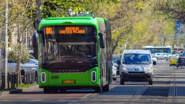 Un autobuz verde circulă pe un drum cu șine de tramvai, având afișaj digital cu numărul 86 și textul Cartier Pajura.