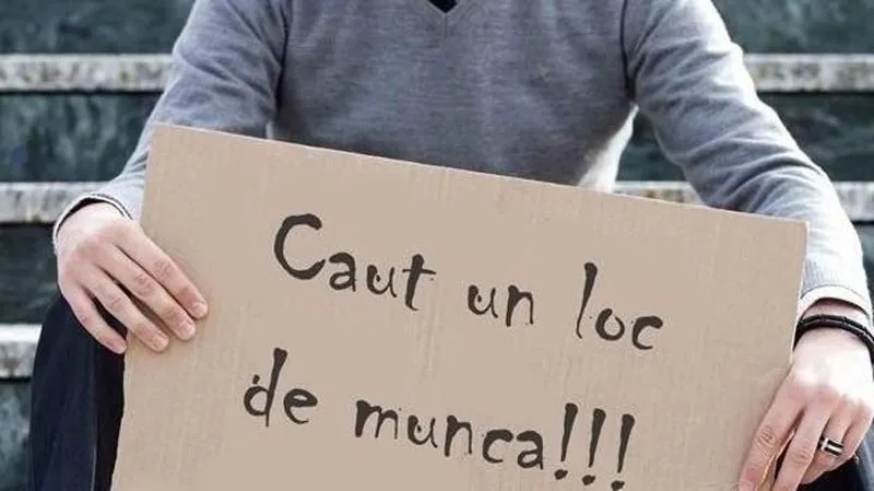 O persoană în tricou gri ține un carton pe care este scris textul cu caractere negre.