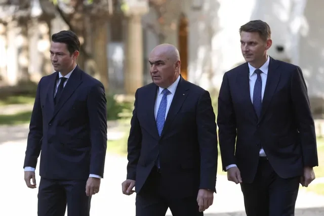 Trei bărbați în costume închise și cravate merg pe o cărare lângă o clădire cu coloane.