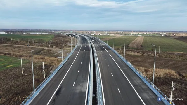 O autostradă cu două caraje separate de o barieră metalică traversează un peisaj de câmpie sub un cer înnorat.