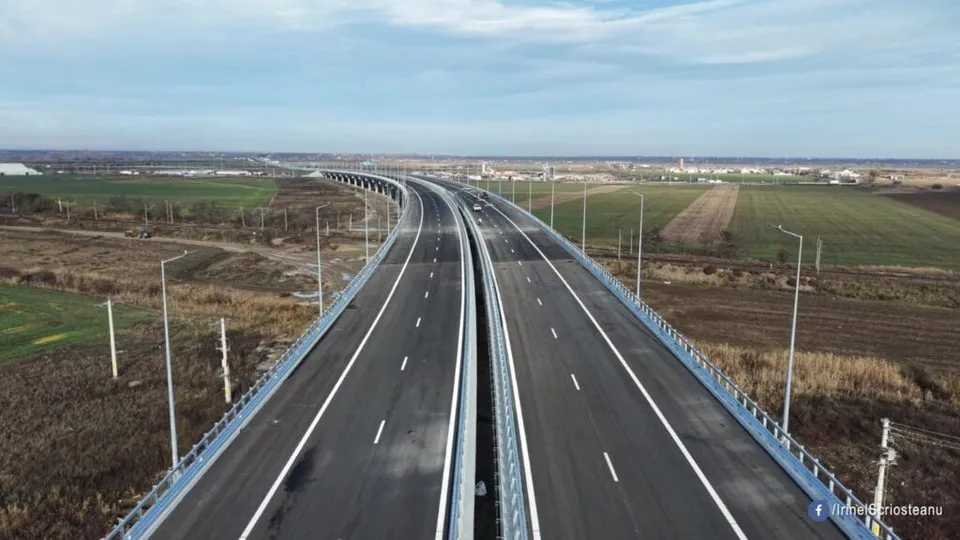 O autostradă cu două caraje separate de o barieră metalică traversează un peisaj de câmpie sub un cer înnorat.