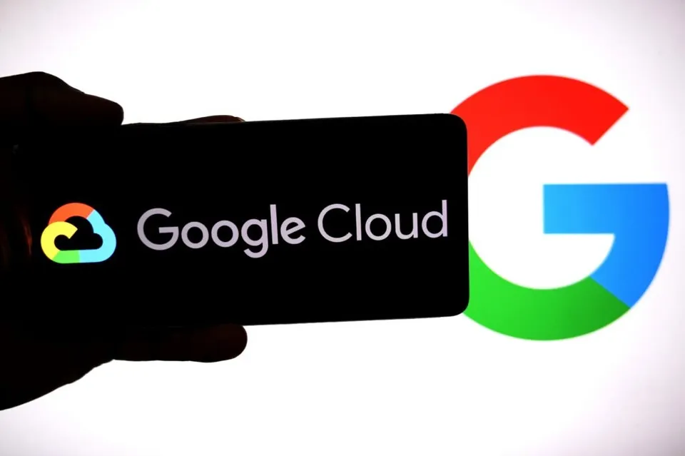 O mână ține un smartphone care afișează logoul și textul Google Cloud pe un fundal negru, lângă un simbol Google de dimensiuni mari.