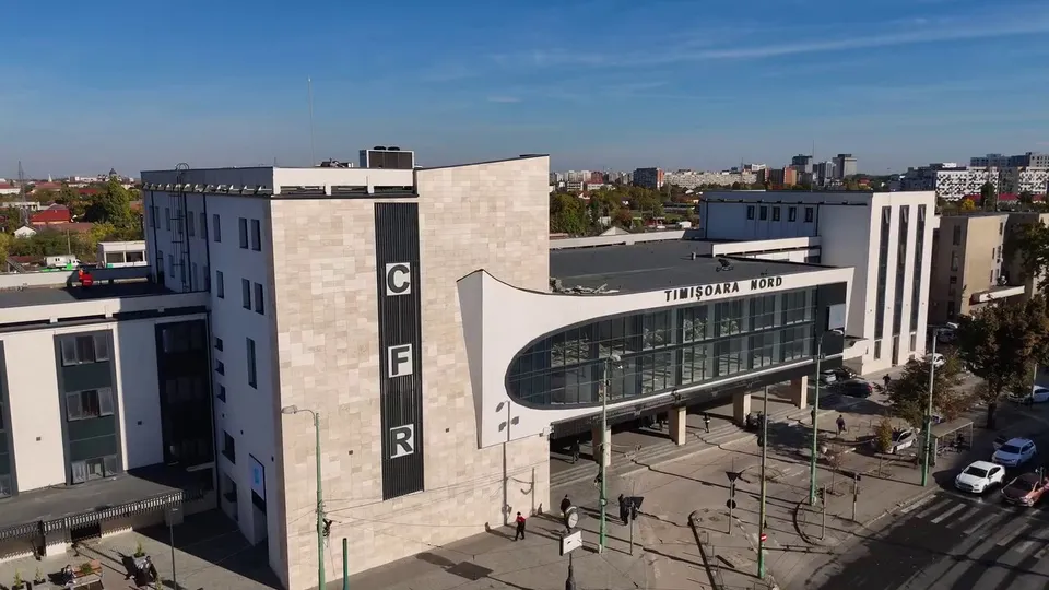 O clădire de călători cu fațadă de piatră deschisă, un element curbat cu ferestre mari și inscripția TIMIȘOARA NORD, sub un cer senin.
