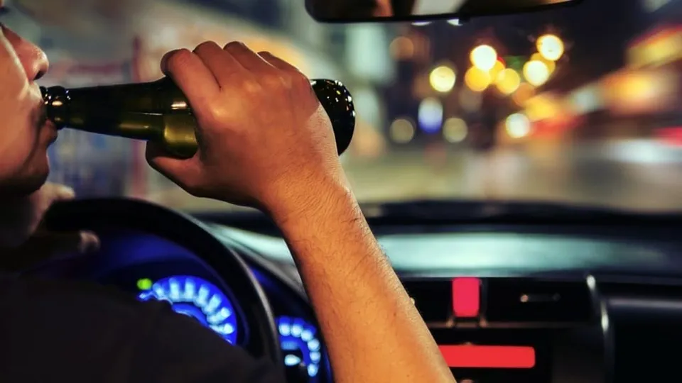 Un bărbat ține un aparat de testare în apropierea gurii, stând la volanul unei mașini pe timp de noapte.