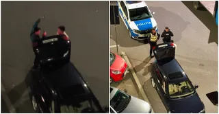 Două persoane stau lângă un autoturism negru deschis, în timp ce o mașină de poliție și doi polițiști sunt poziționați pe carosabil.