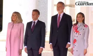 Patru persoane stau în rând, două femei purtând haine roz și gri, iar doi bărbați purtând costume închise și cravate.