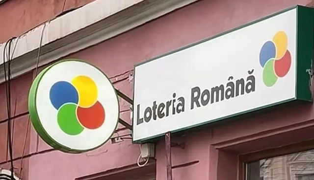 Un panou dreptunghiular alb cu textul Loteria Română și un logo colorat este montat pe o clădire de culoare roz.