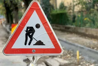 Un semn de circulație triunghiular cu margini roșii și simbolul unei persoane lucrând cu o lopată este montat pe un stâlp.
