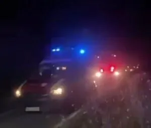 Două vehicule cu lumini aprinse sunt vizibile pe un drum în timpul nopții, sub lumini albastre de semnalizare.