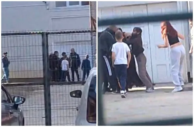 Un grup de persoane este adunat în fața unei clădiri lângă un gard metalic și o mașină albă.