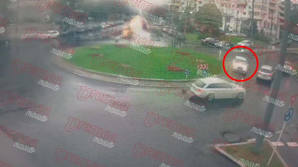 O vedere de sus de pe o stradă cu un sens giratoriu verde, având mai multe mașini parcate sau circulând pe asfaltul umed.