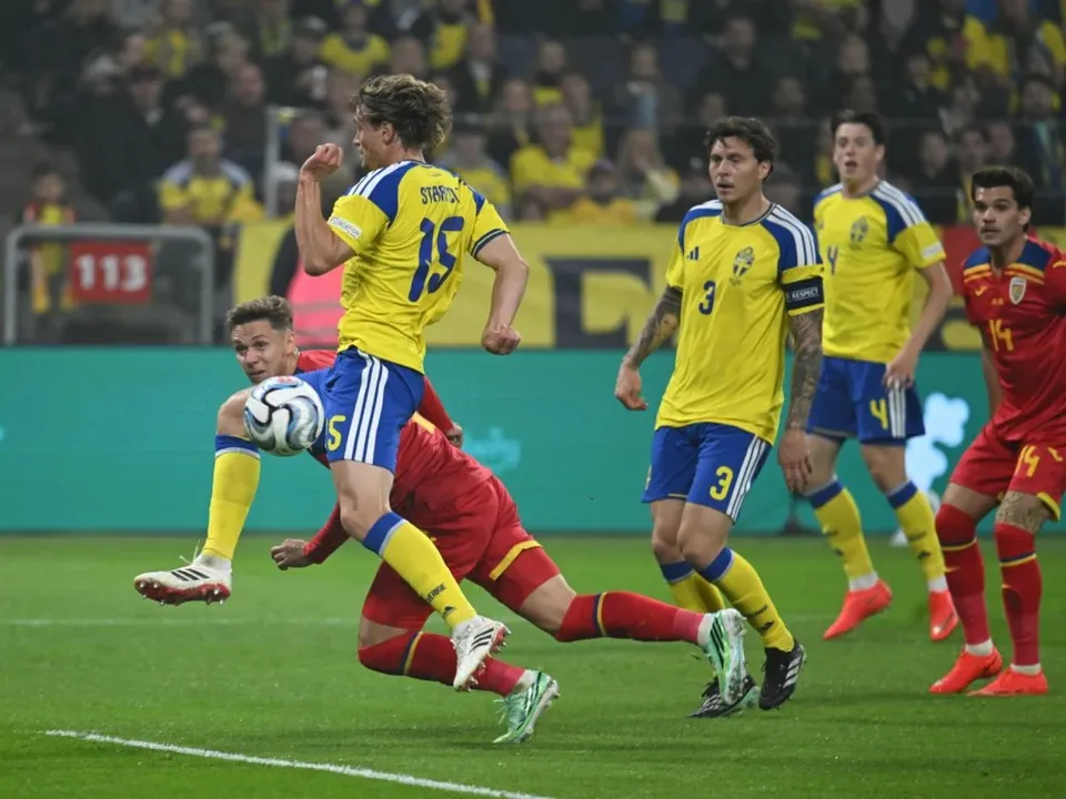 Câțiva jucători de fotbal în echipamente galbene și albastre și roșii se află pe un teren de fotbal verde în timpul unui meci.