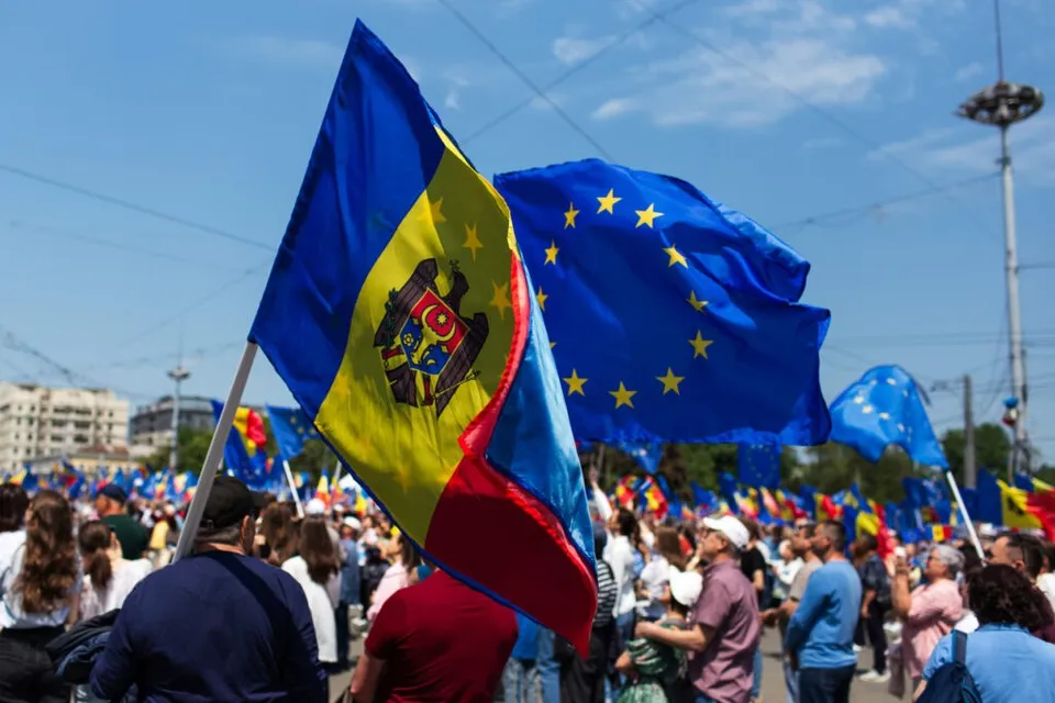 O mulțime de oameni ridică steagurile Moldovei și ale Uniunii Europene sub un cer senin.