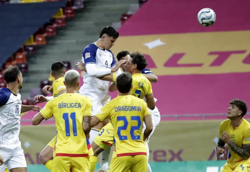 Jucători de fotbal în echipamente albastre și albe și galbene concurează pe un teren de fotbal sub un cer de stadion.