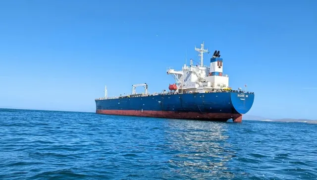 O navă mare de culoare albastră și roșie navighează pe un ocean sub un cer senin.