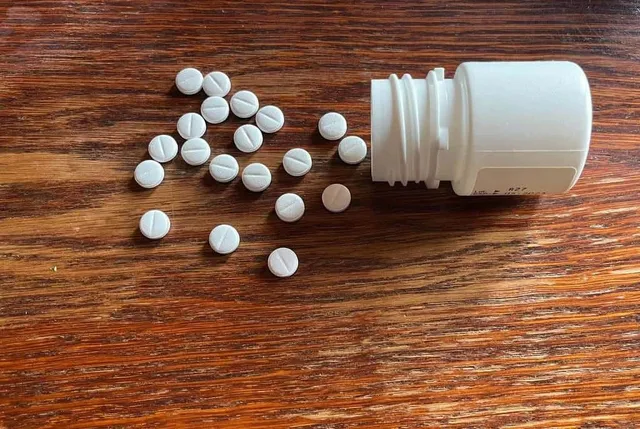 Diverse pastile albe rotunde sunt împrăștiate pe o suprafață de lemn lângă un flacon de plastic alb.
