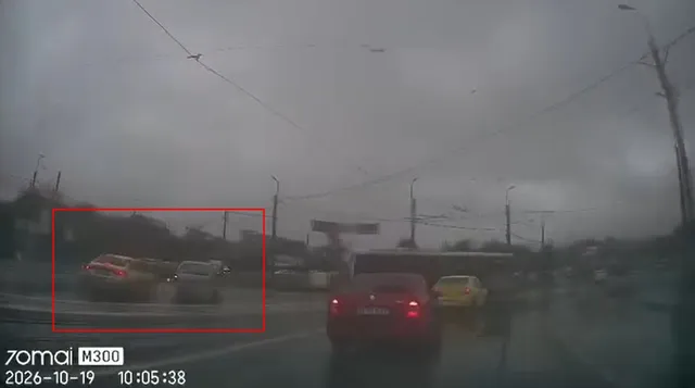Mașini circulă pe un drum asfaltat sub un cer gri însemnat de cabluri aeriene și stâlpi de iluminat.
