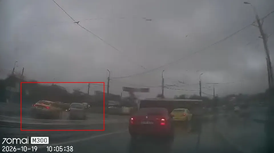 Mașini circulă pe un drum asfaltat sub un cer gri însemnat de cabluri aeriene și stâlpi de iluminat.