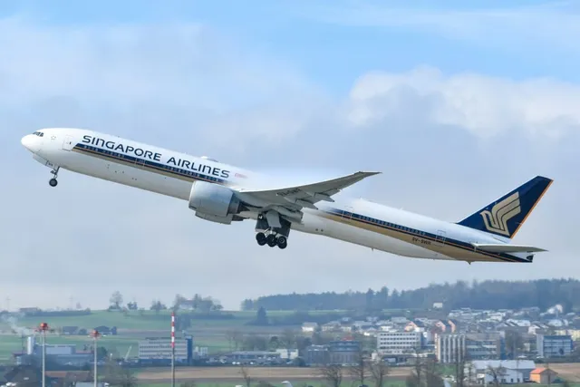 Un avion de pasageri alb cu inscripția Singapore Airlines decolă de pe o pistă deasupra unui peisaj cu clădiri și copaci.