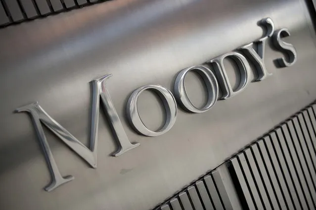 Un logo metalic cu textul Moody's este montat pe o suprafață metalică gri cu linii striate.
