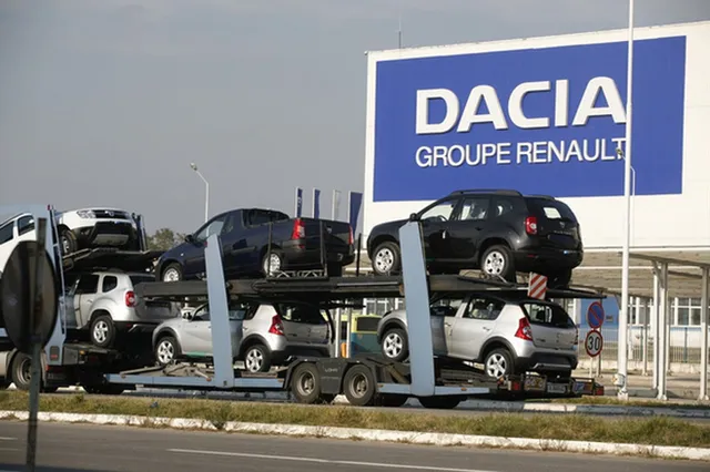Mai multe mașini de culori diferite sunt transportate pe un remorcă de tip platformă pe un drum asfaltat.