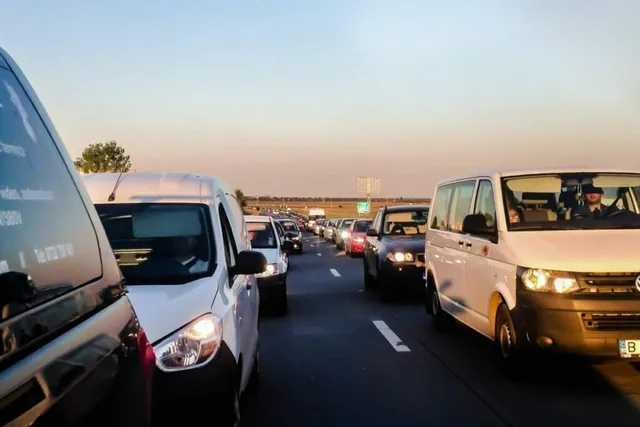 Mai multe autovehicule albe și închise culori sunt așezate în rând pe o bandă de rulare sub un cer senin.
