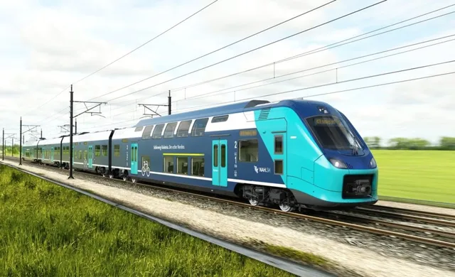 Un tren albastru și turcoaz circulă pe o cale ferată lângă un câmp verde sub un cer înnorat.