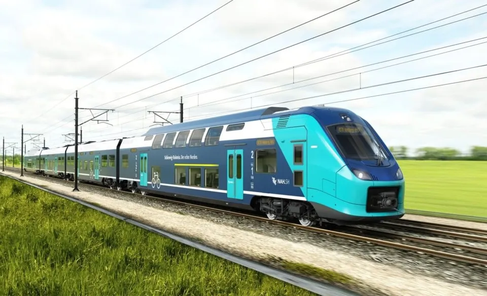 Un tren albastru și turcoaz circulă pe o cale ferată lângă un câmp verde sub un cer înnorat.